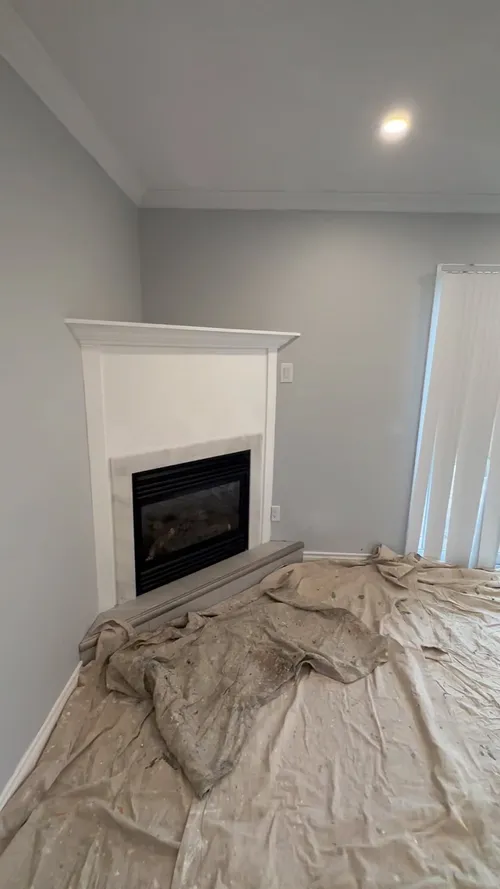Grey walls and a white corner fireplace mantel, drop cloths on the floor