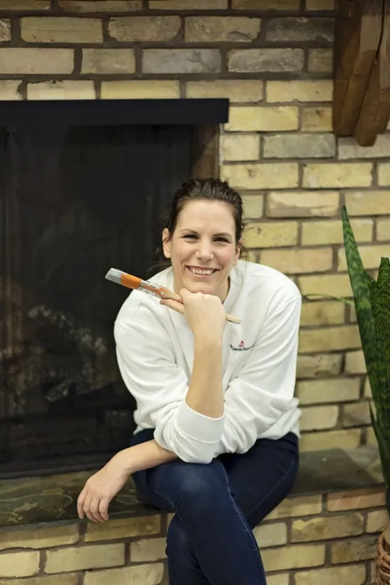 Sarah Meissner sitting by a brick fireplace with a paintbrush