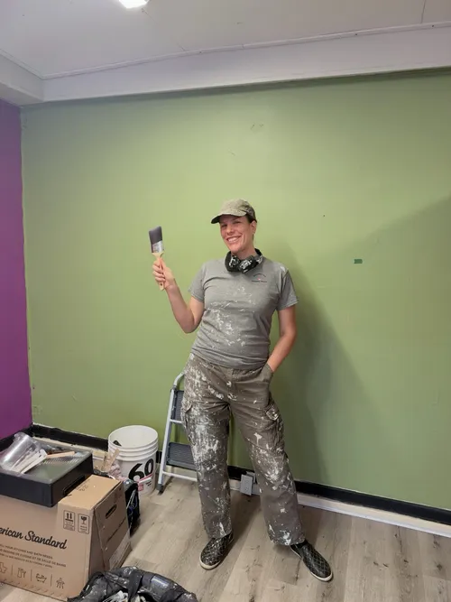 Sarah Meissner in paint-splattered work clothes holding a brush on a job