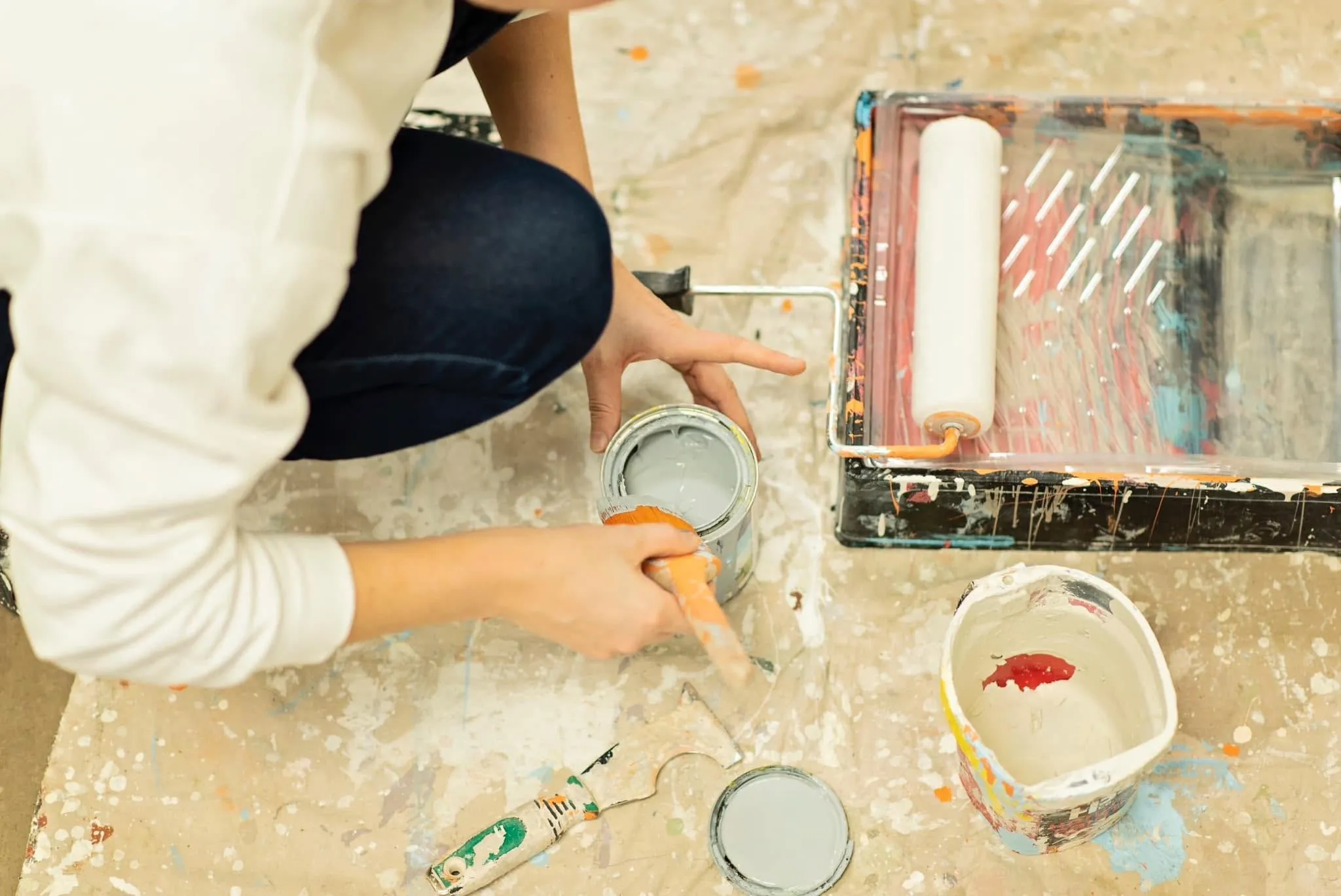 Sarah loading her brush with grey paint beside a roller tray on a drop cloth
